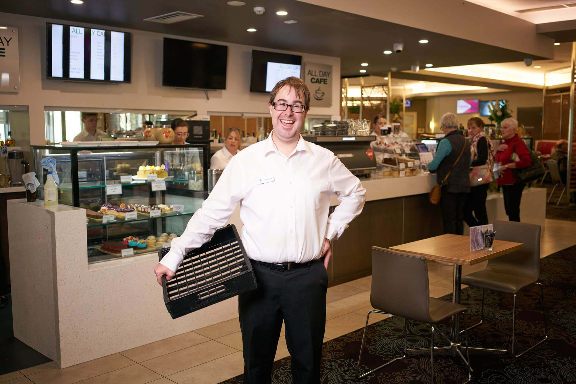 Pat smiling with a tray in front of a cafe counter