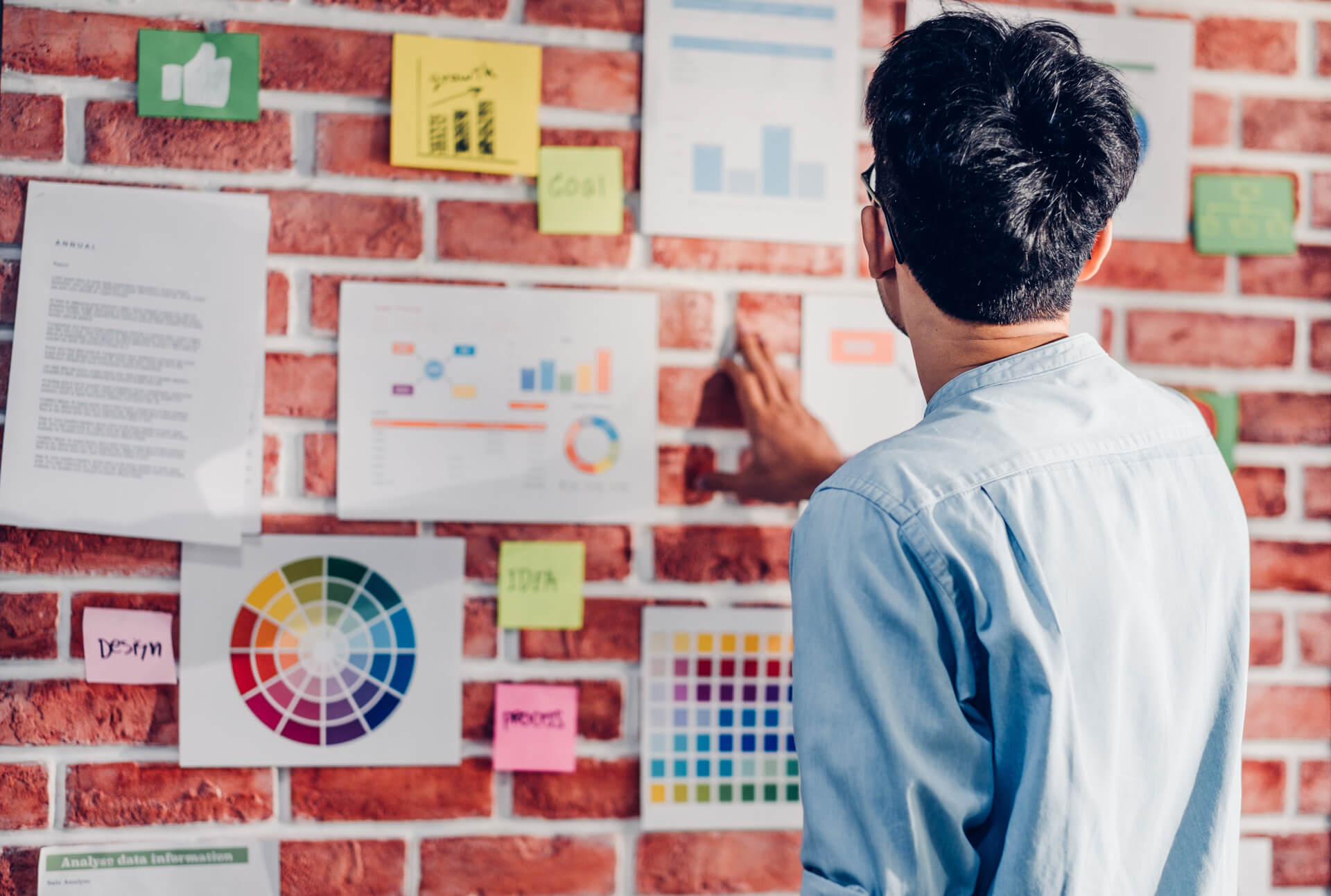 A person examining a wall filled with numerous sticky notes, appearing contemplative