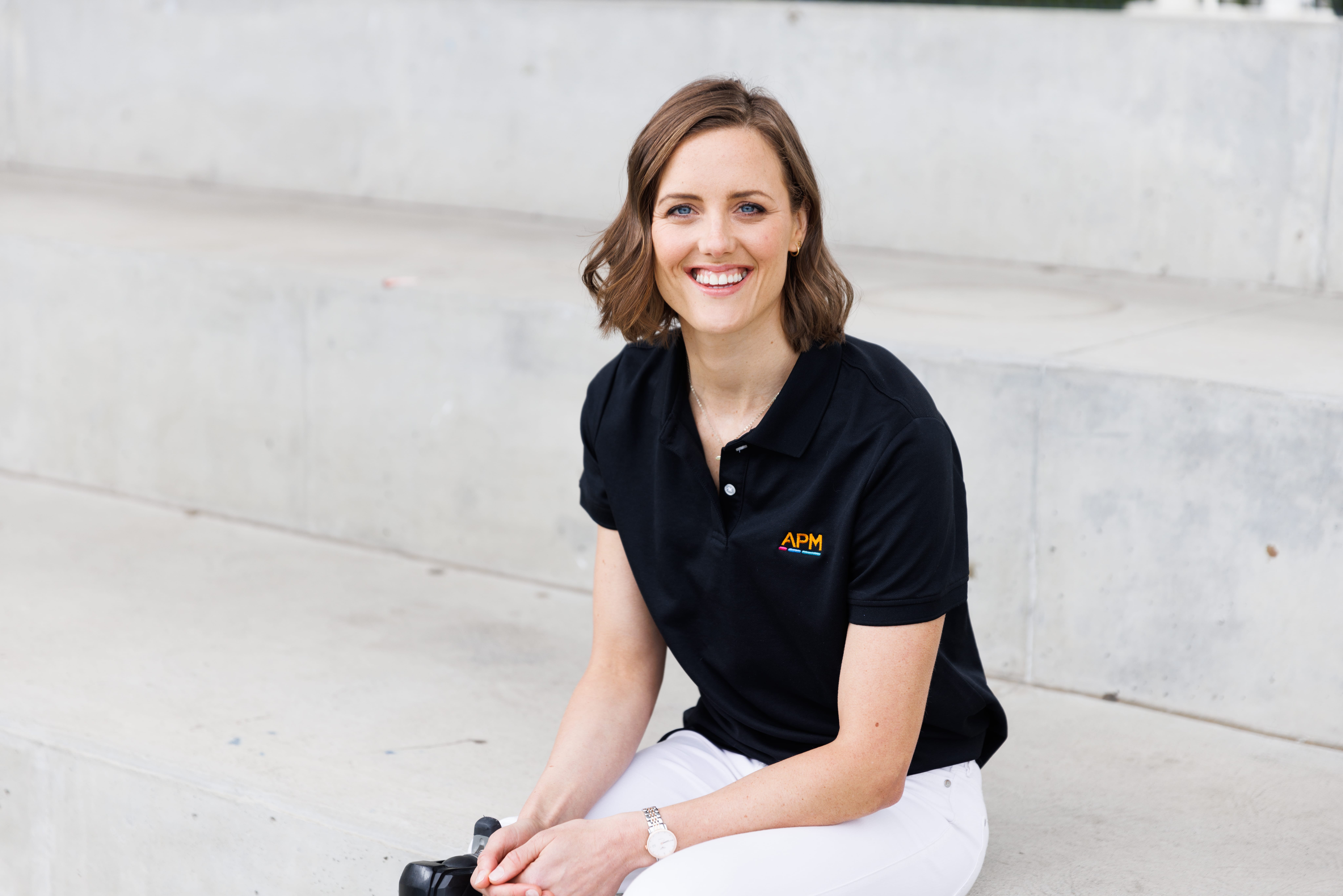 Ellie Cole smiles in a black APM polo