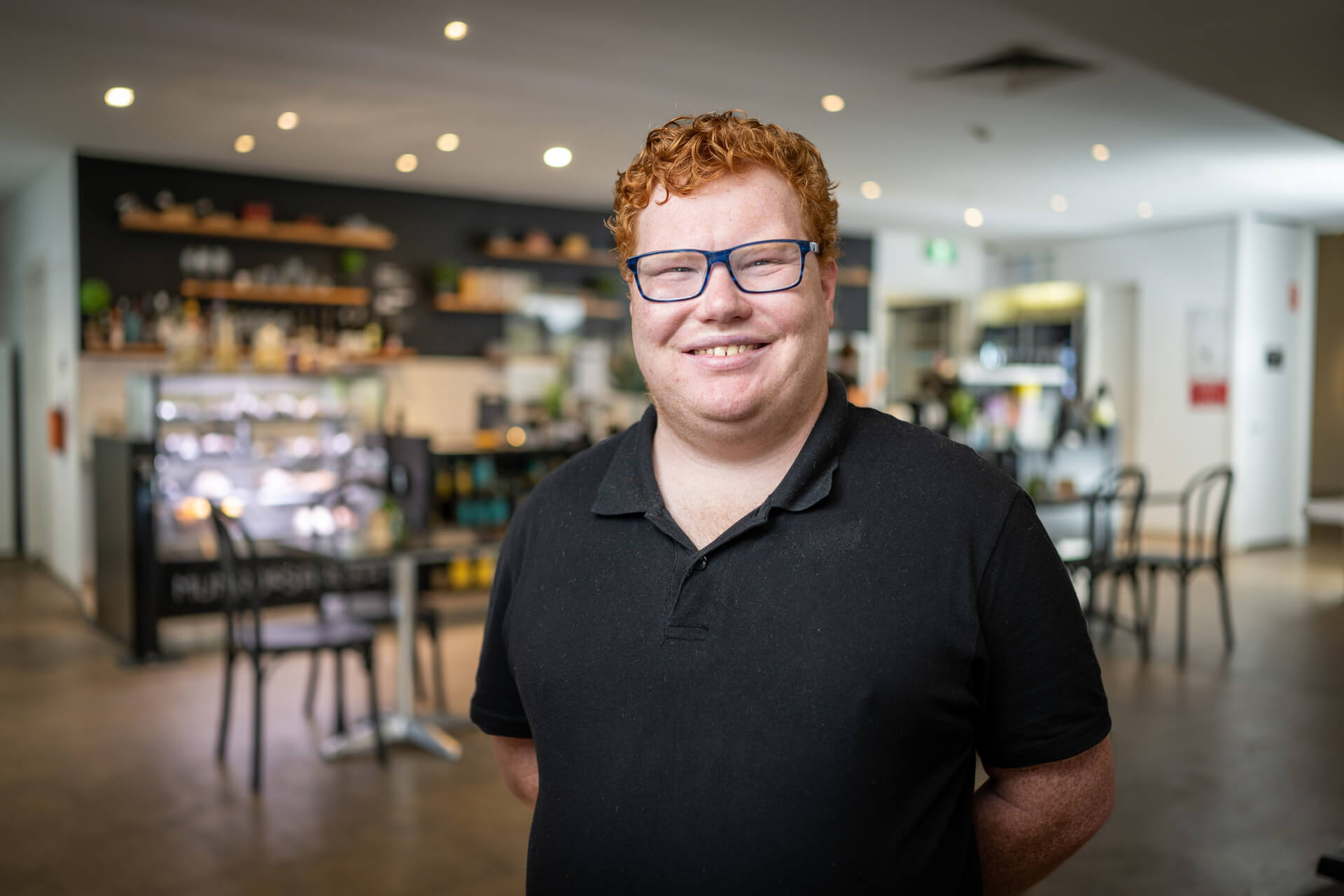 Andrew a DES participant smiles in his cafe workplace in a black polo