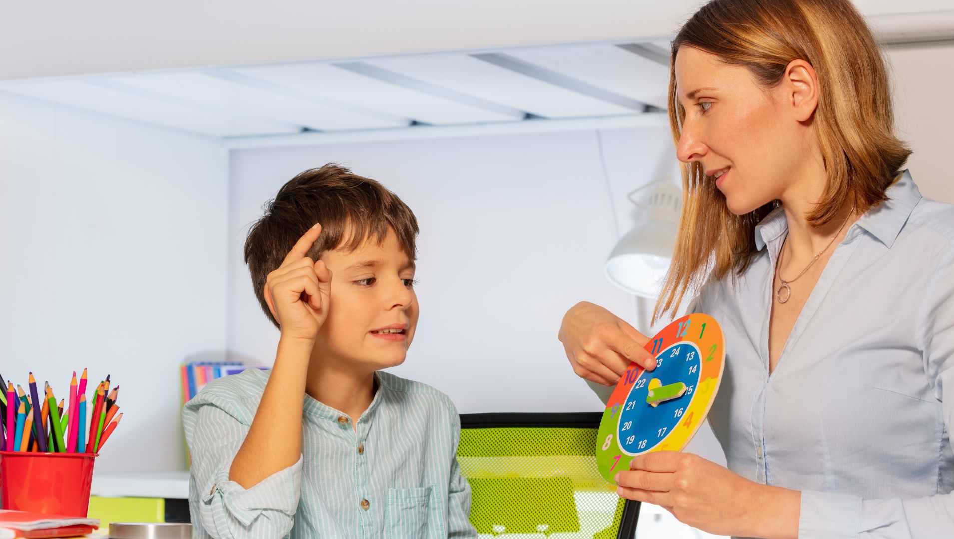 Young autistic boy looks at a clock held by a therapist