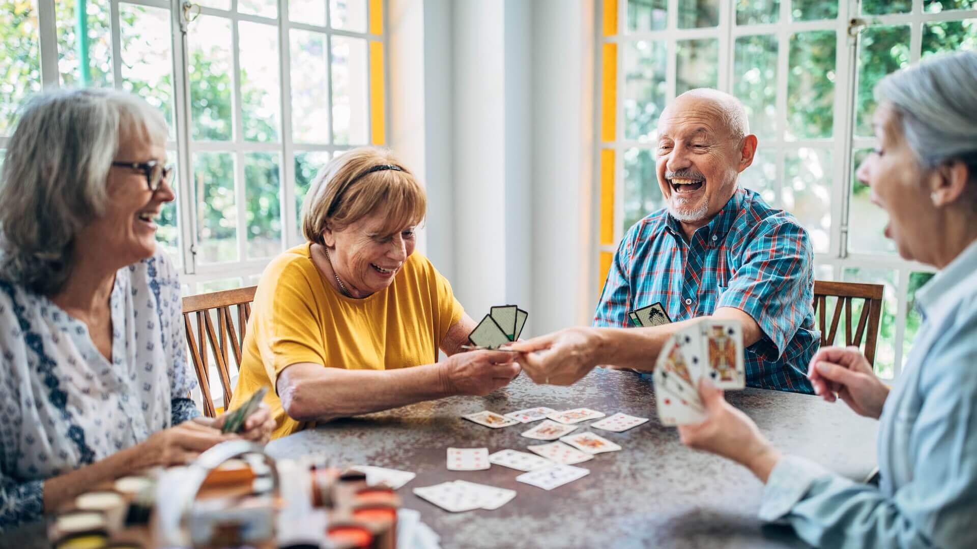 Four smiling older adults playing cards