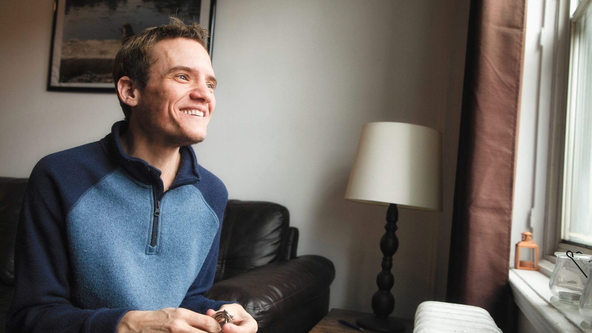 A smiling man at home looking out a window